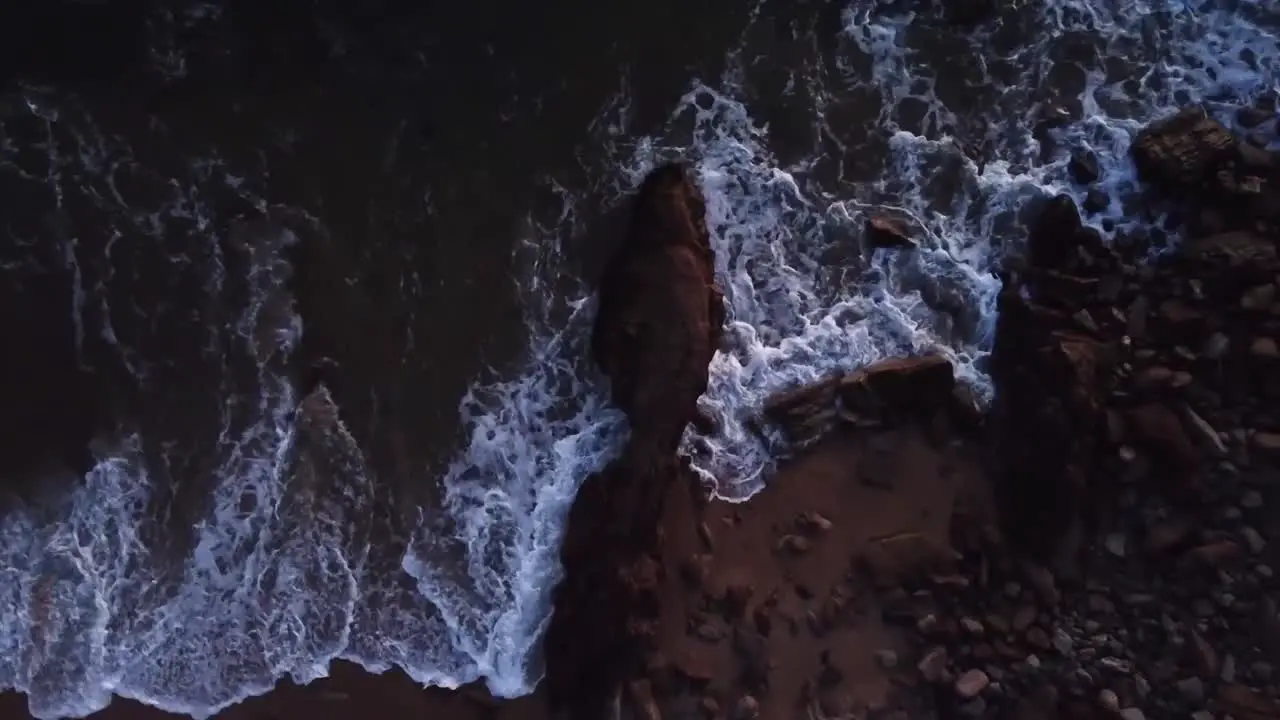 Top view drone hoovering a rock at the beach water hitting rock during sunset