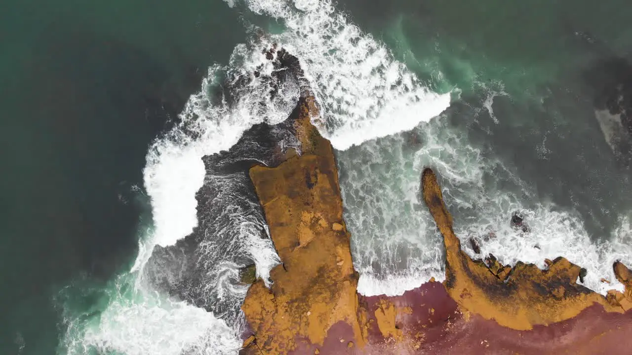 Descending spinning aerial shot of waves crushing in to a huge cliff at the ocean coastline