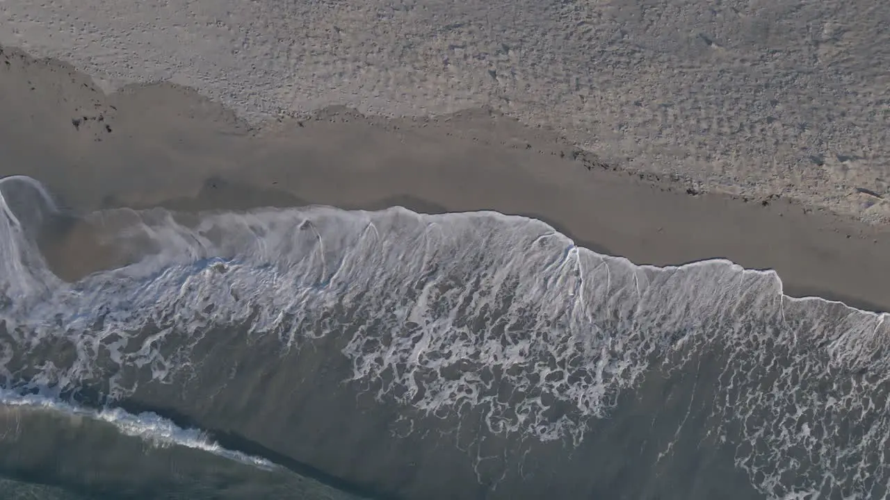 Foamy ocean waves hitting sandy beach aerial top down shot