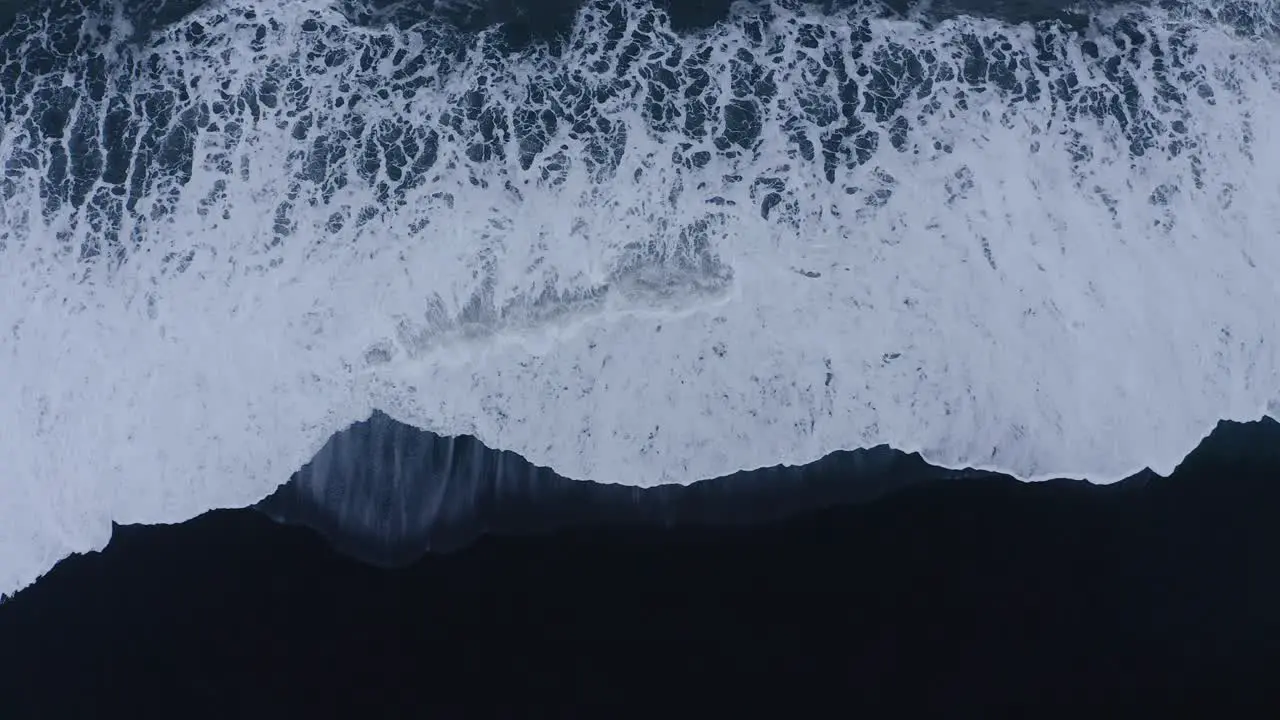 Powerful Atlantic waves rolling in on black sand beach in Iceland aerial ascending straight down