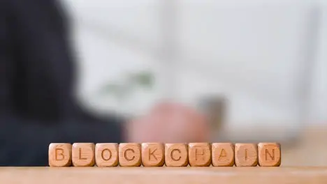 Business Concept Wooden Letter Cubes Or Dice Spelling Blockchain With Office Person Using Mobile Phone In Background