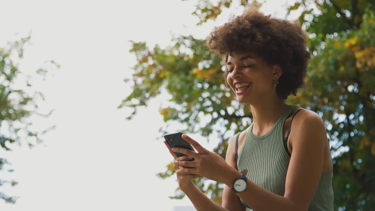 Smiling Young Woman Outdoors Laughing As She Messages On Mobile Phone