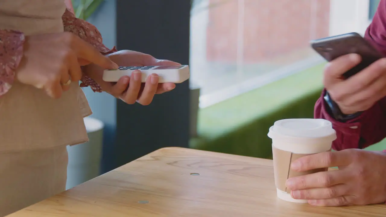 Close Up Of Man Making Contactless Purchase In Coffee Shop Using Mobile Phone