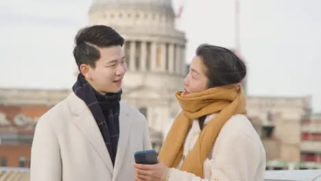 Young Asian Couple On Holiday Walking Across Millennium Bridge With St Pauls Cathedral In Background