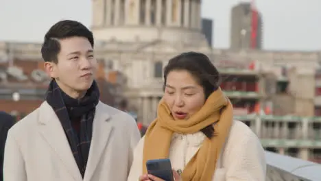 Young Asian Couple On Holiday Walking Across Millennium Bridge With St Pauls Cathedral In Background 2