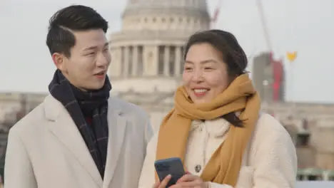 Young Asian Couple On Holiday Walking Across Millennium Bridge With St Pauls Cathedral In Background 3