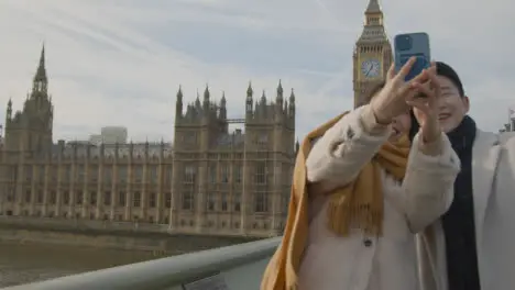 Young Asian Couple On Holiday Posing For Selfie In Front Of Houses Of Parliament In London UK 3