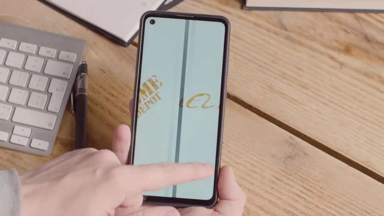 Person Holding Mobile Phone On Desk With Screen Showing Brand Logos For Amazon Alibaba The Home Depot Costco Walmart and Ikea