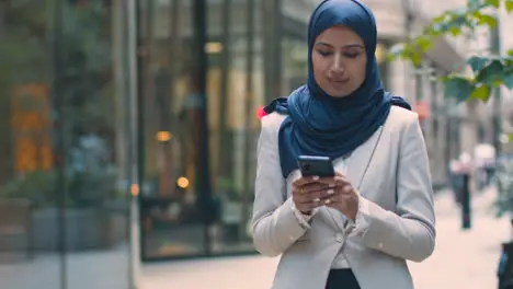 Muslim Businesswoman Checking Messages On Mobile Phone Standing Outside Office In City 2