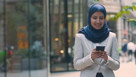 Muslim Businesswoman Checking Messages On Mobile Phone Standing Outside Office In City 3