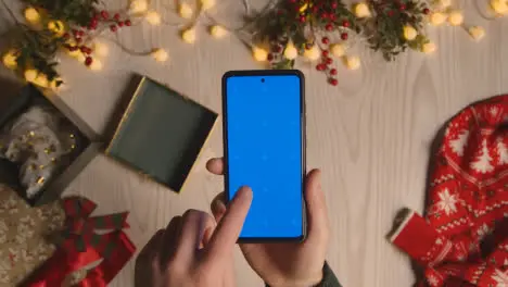 Overhead Shot Of Person Holding Blue Screen Mobile Phone With Christmas Decorations And Wrapping 1