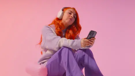 Studio Shot Of Young Gen Z Woman Wearing Headphones Streaming Music To Mobile Phone 2