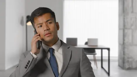 Serious Businessman In Suit Taking Call On Mobile Phone In Modern Open Plan Office