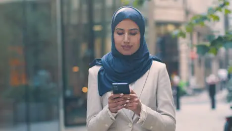 Muslim Businesswoman Checking Messages On Mobile Phone Standing Outside Office In City 1