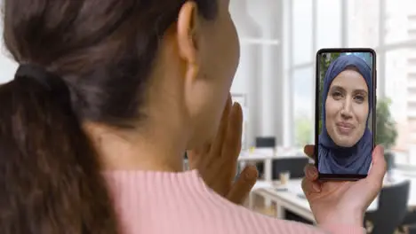 Close Up Of Businesswoman In Office Having Video Call With Female Muslim Colleague On Mobile Phone