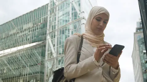 Muslim Businesswoman Checking Messages On Mobile Phone Standing Outside Office In City