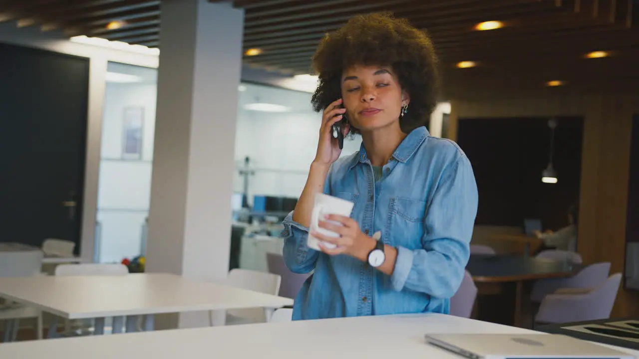 Businesswoman Standing In Modern Open Plan Office Talking On Mobile Phone