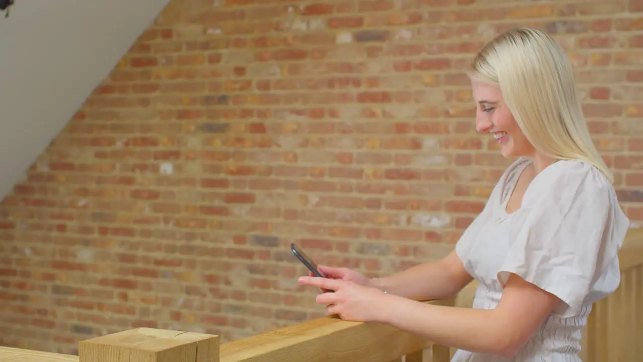 Young Woman Standing By Wooden Staircase At Home Making Video Call On Mobile Phone