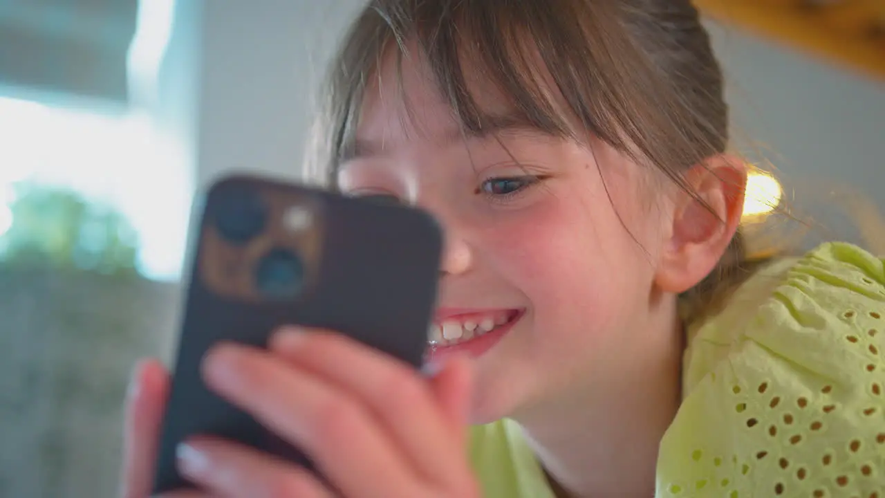 Smiling Girl In Bedroom Lying On Bed Using Mobile Phone