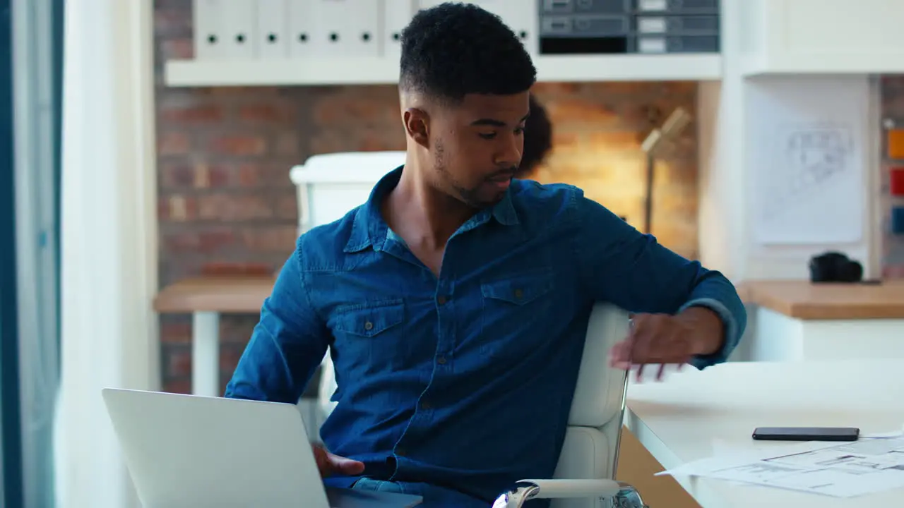 Young Businessman Using Laptop Working At Desk In Office Taking Call On Mobile Phone