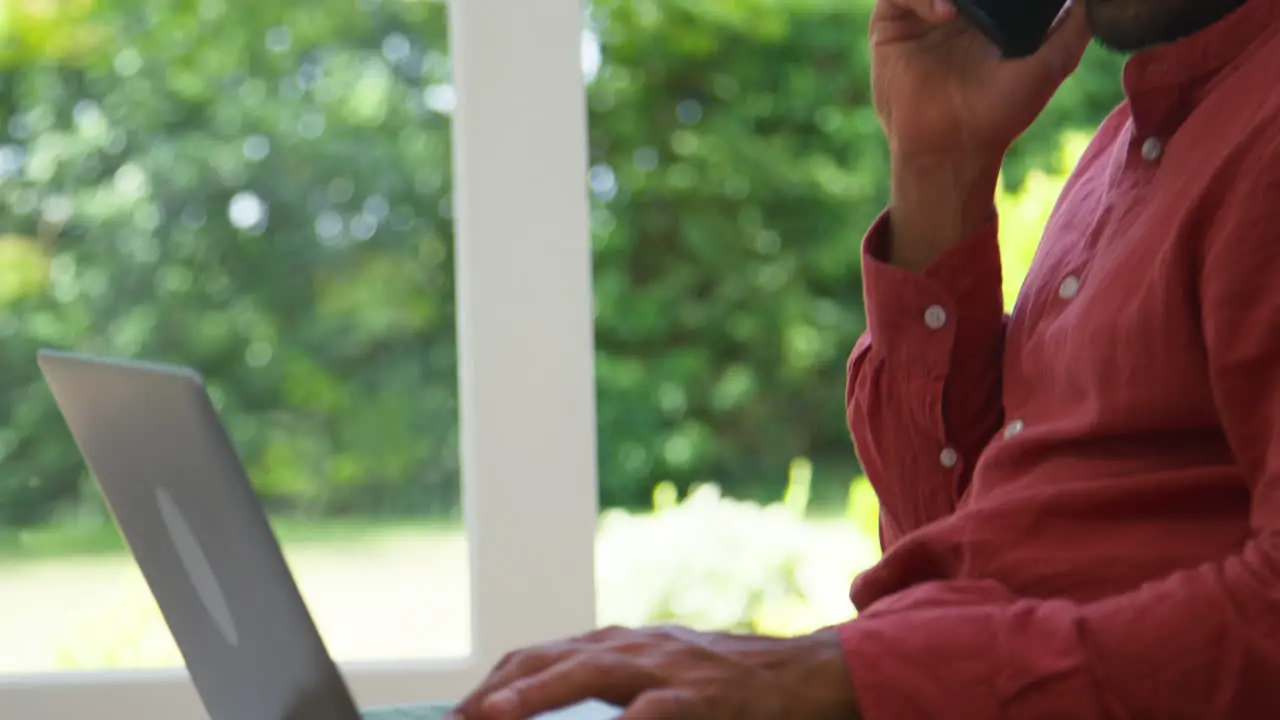 Close Up Of Man Working From Home Sitting On Floor In Lounge Using Laptop And Mobile Phone