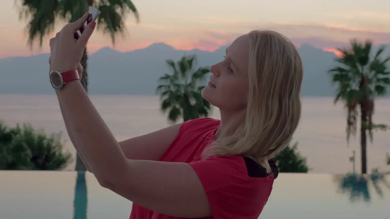 A young woman taking selfies by the beautiful evening scenery near the pool