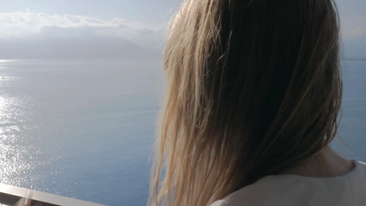 A woman on a balcony talking to a phone and a sea view behind her