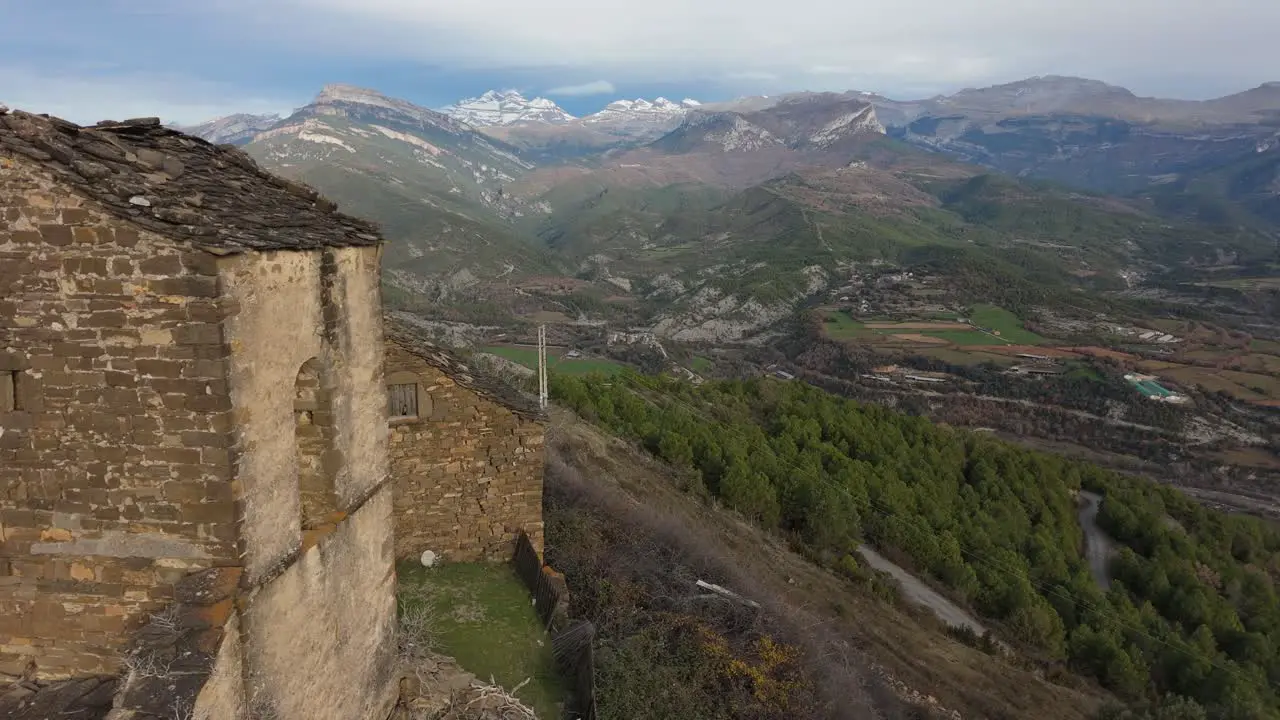 Drone shot from an abandoned church in Muro de Bellos Spain with a beautiful green landscape and a snowy mountain as a background