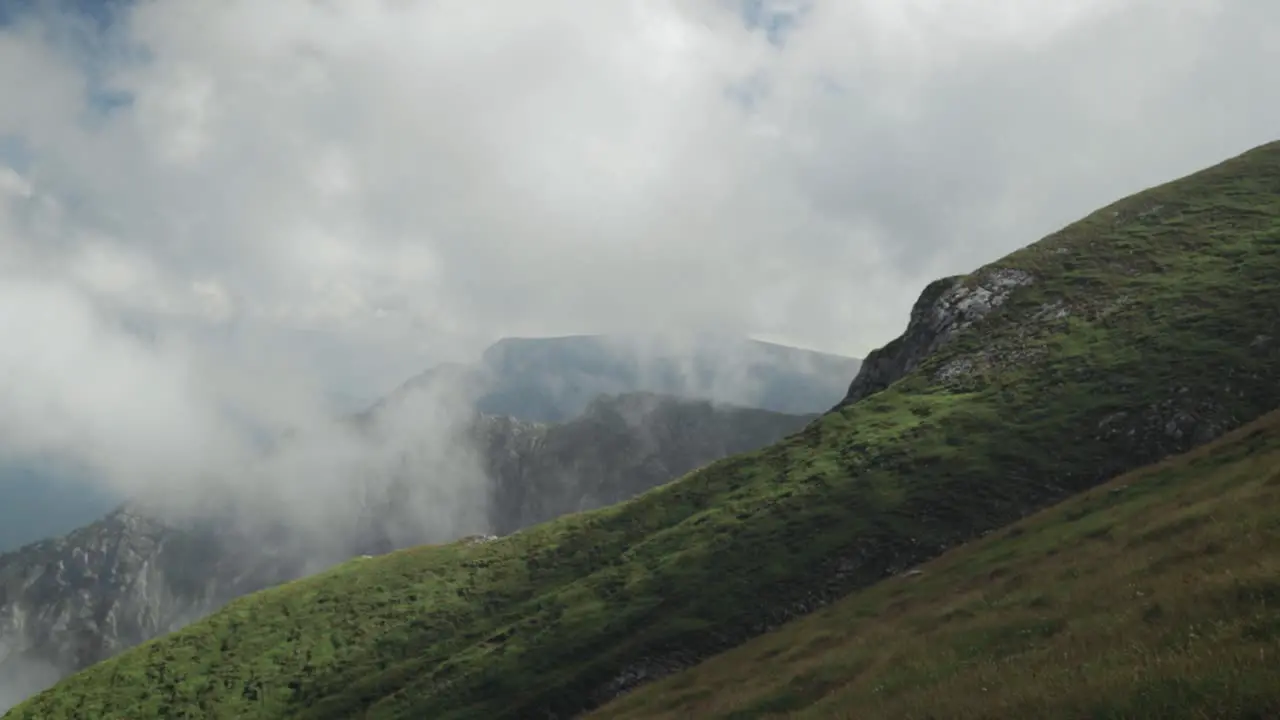 Pan left to right of a mountain steep with low clouds and mountain peaks in the background