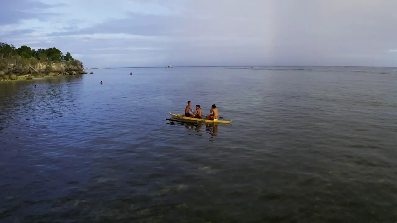 aerial pan shot of three Philipino boys in the boat swimming in the sea at Panglao