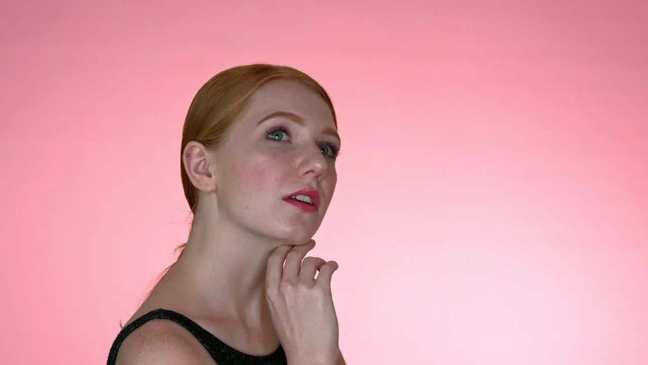 A close-up of a woman framing her face with her hand looking into the camera with her mouth slightly open on a seamless studio background