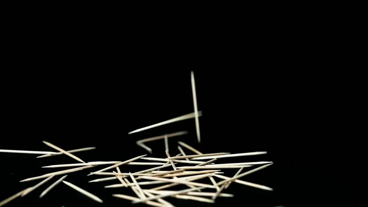 light wooden toothpicks fall in front of black background on dark background slow motion