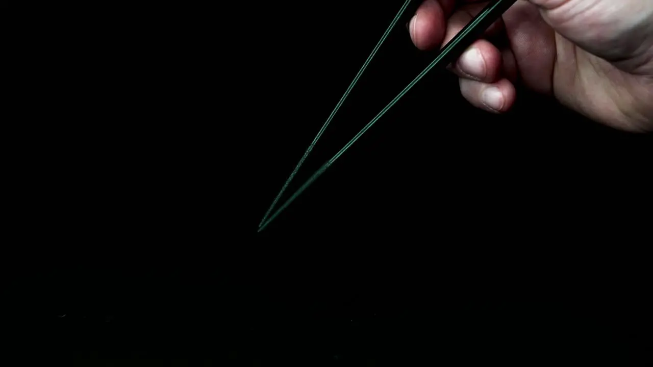 one hand moves two black chopsticks in the typical posture against a black background slow motion