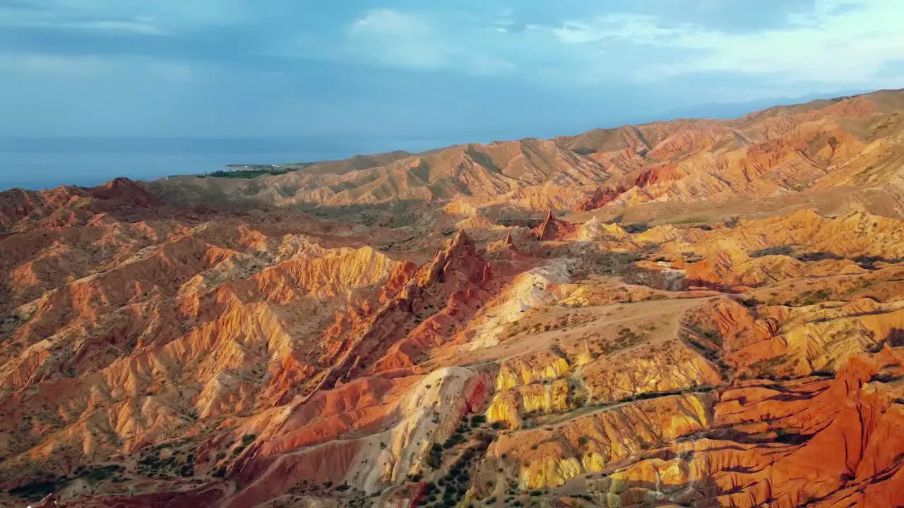 Drone flying over red canyon mountains at sunset capturing rugged peaks and stunning colours reflecting on the lake with stormy clouds adding a dramatic touch