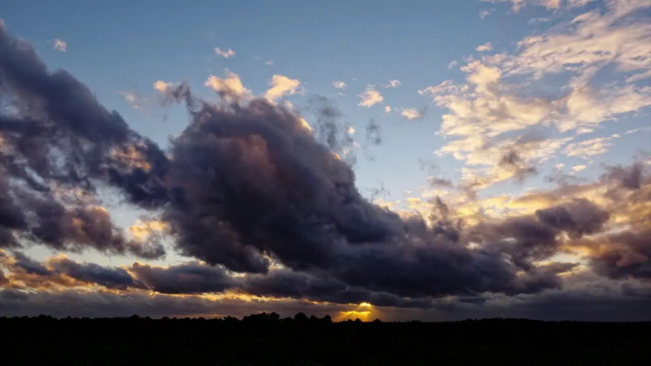 Timelapse taken by drone shows clouds colored by the rays of the sunset with changing shapes and colors while flying over the landscape offering a breathtaking view of the clouds and the sunset