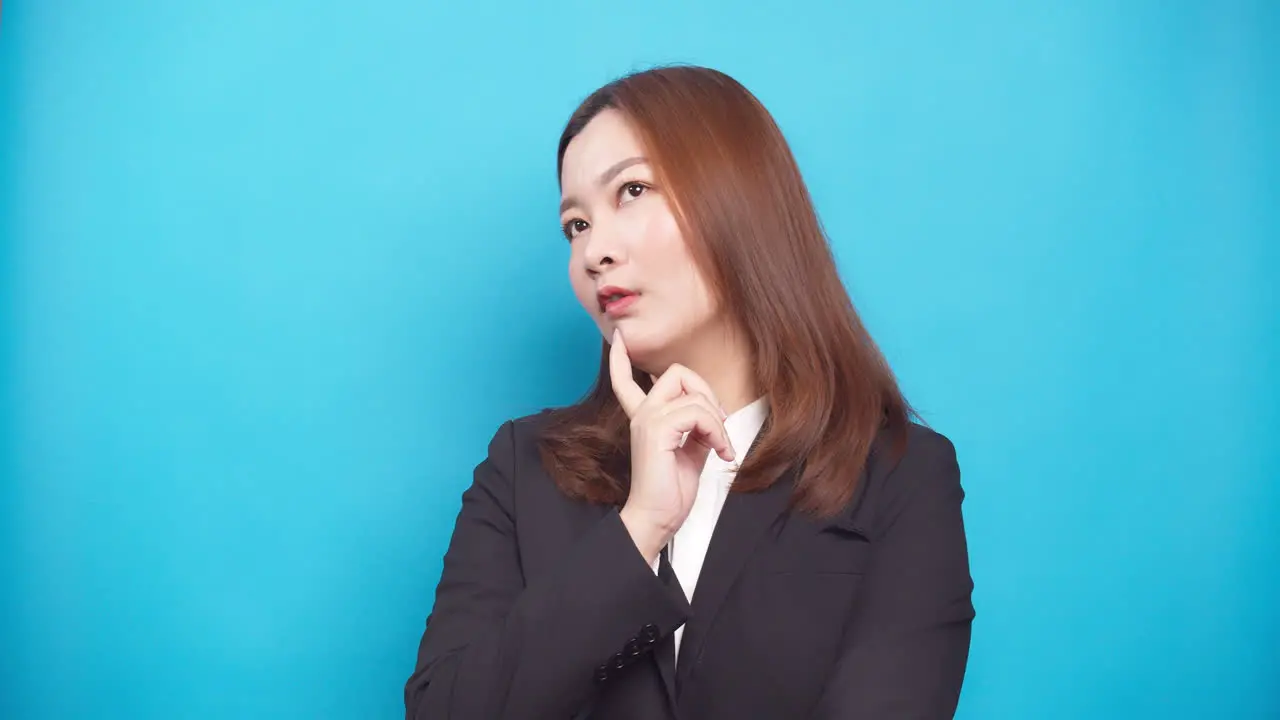 Uncertain young businesswoman thinking and looking up having idea enlightenment standing isolated over a blue background