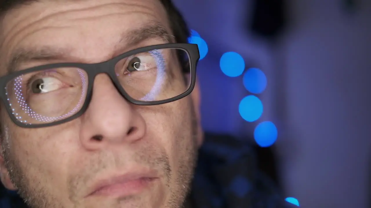 A man with glasses looking at the camera and all around then smiling with a blue defocused background