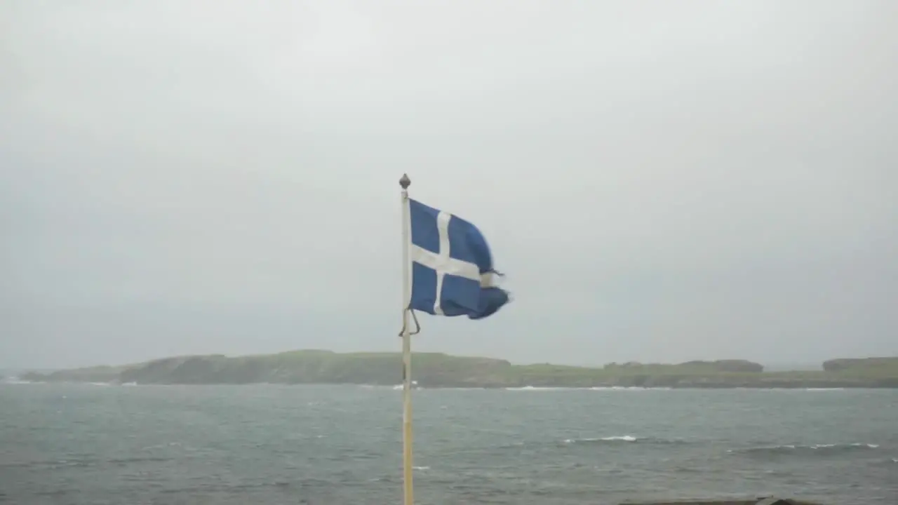 Worn Scottish flag flying in strong stormy winds on remote Scottish island with fog behind