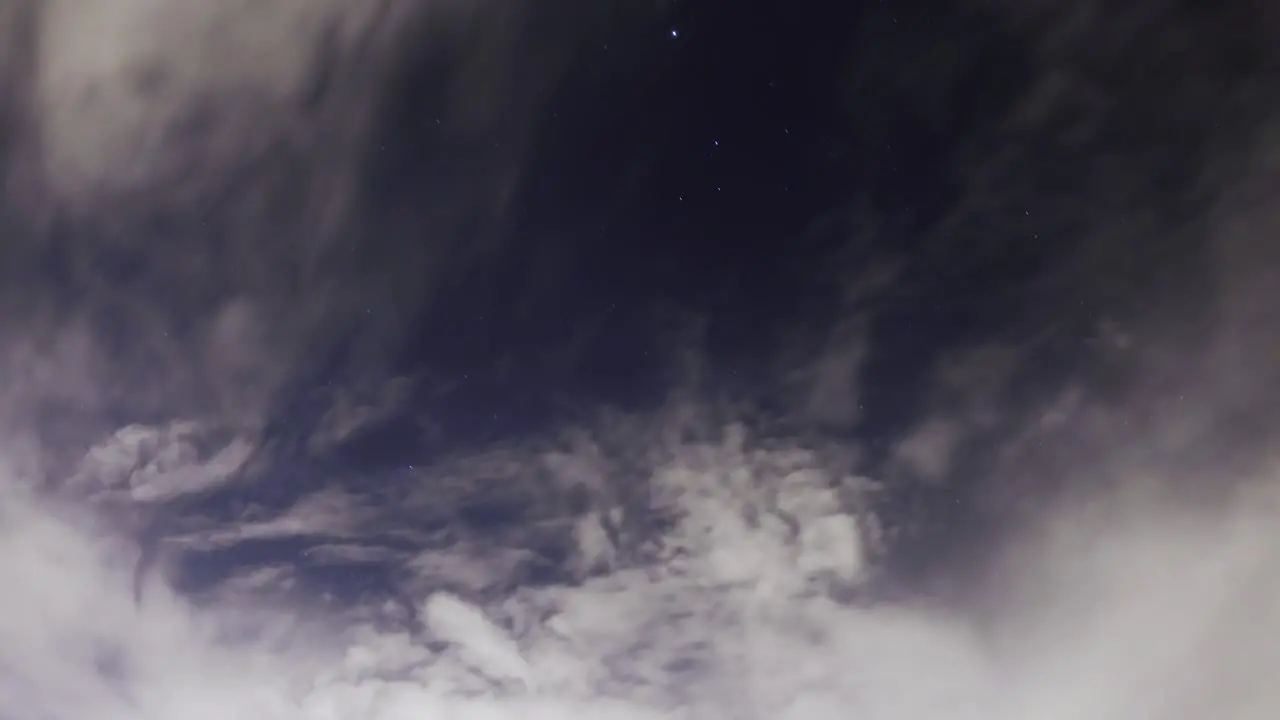 Storm clouds build at nighttime as stars trace across the sky in the background