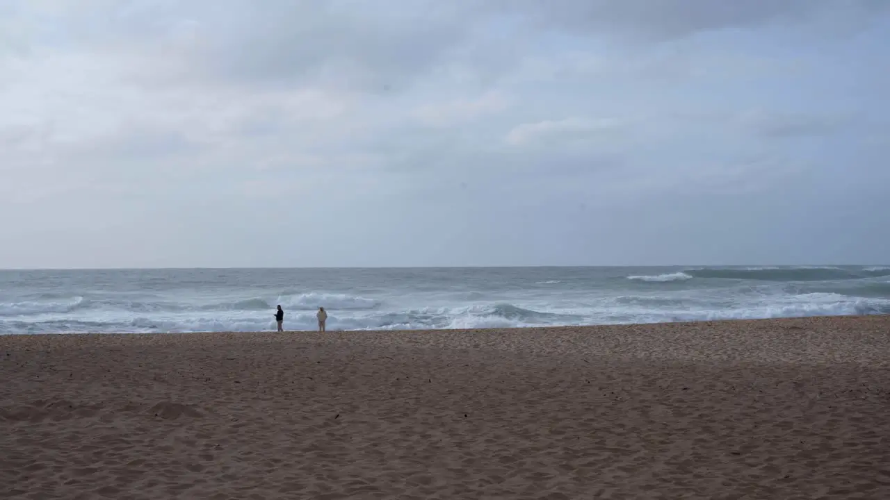 Tourists walking on a beach with violent sea waves crashing at Praia da Adraga in Portugal