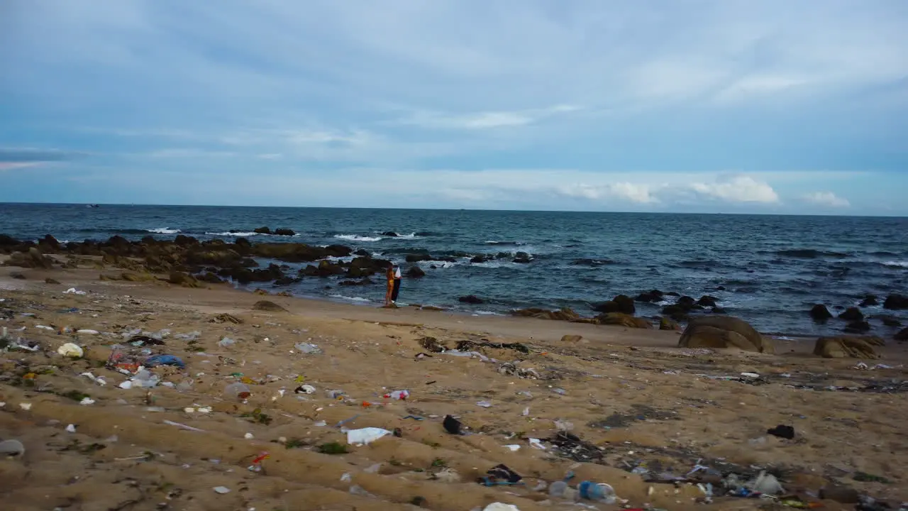 Drone approach female tanned surfer standing on tropical beach with plastic waste garbage trash toxic pollution climate change concept