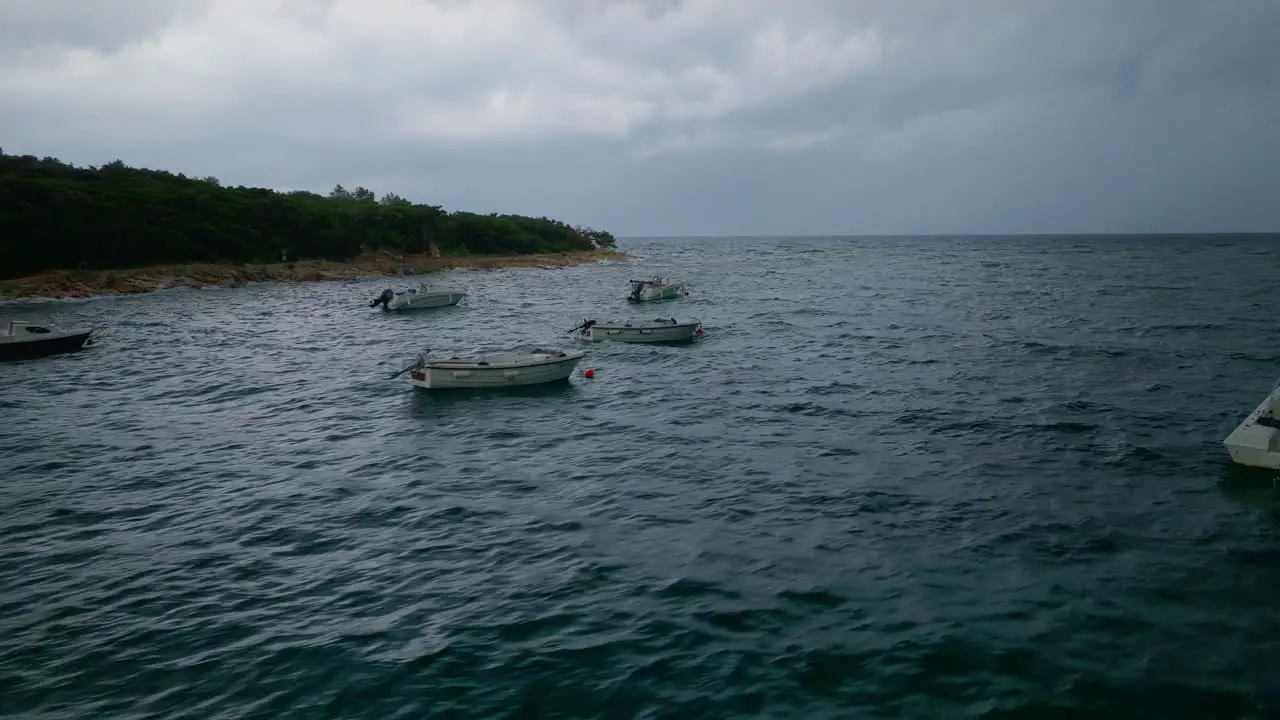 Aerial trucking pan across rocky ocean ripples above small boats anchored off coastline