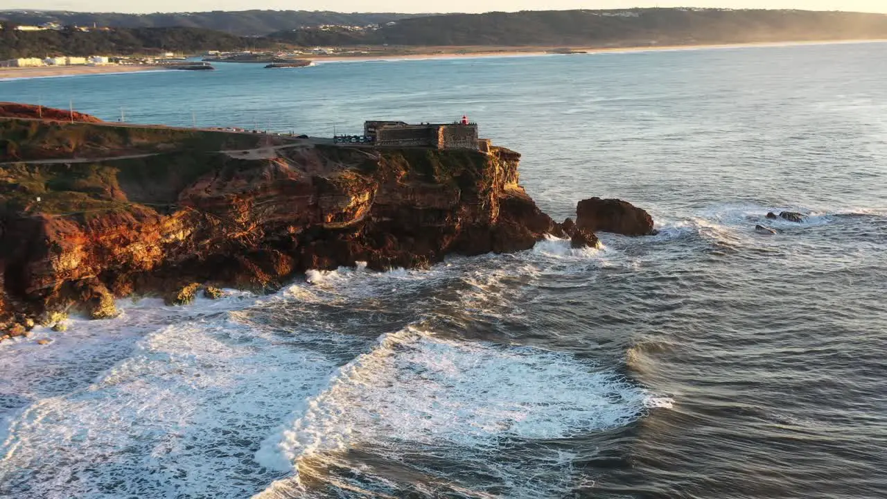 The Nazare Portugal Lighthouse in Praia do Norte during golden hour sunset Aerial dolly in from side