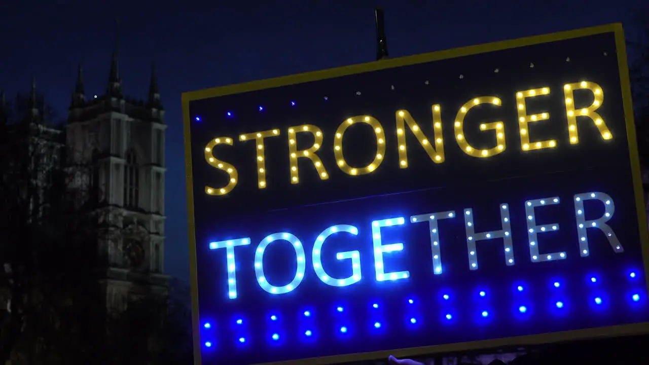 A passenger plane passes behind an illuminated placard that says Stronger Together” and Westminster Abbey is seen in the background at night