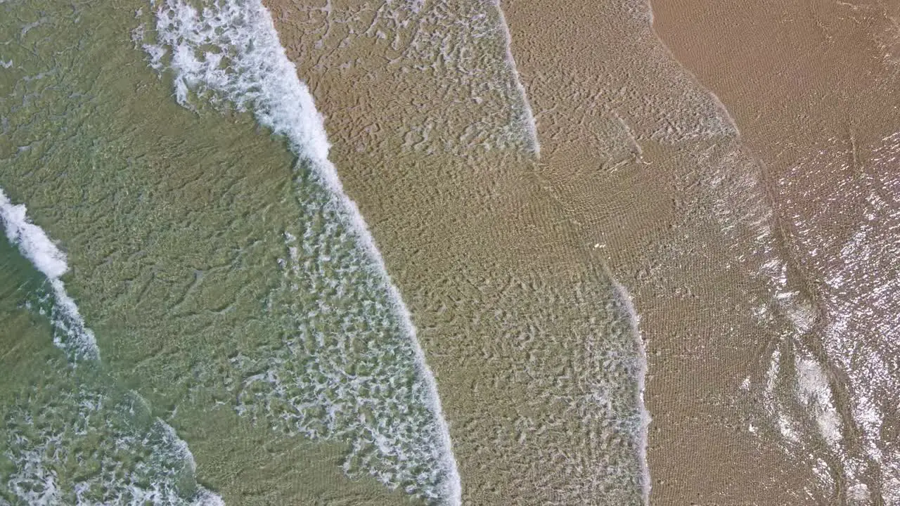 aerial view of small waves breaking on sandy beach