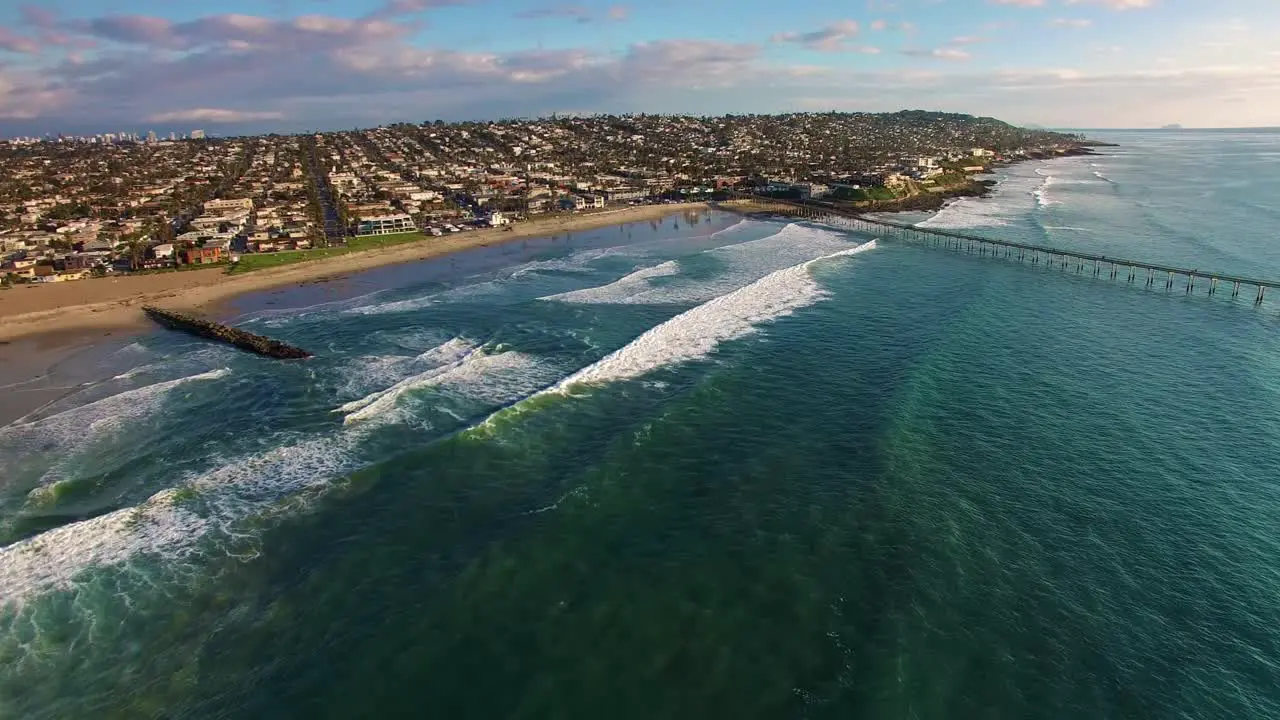 4K aerial drone wide view of California pier and beach town coastline huge blue turquoise Pacific Ocean waves rolling