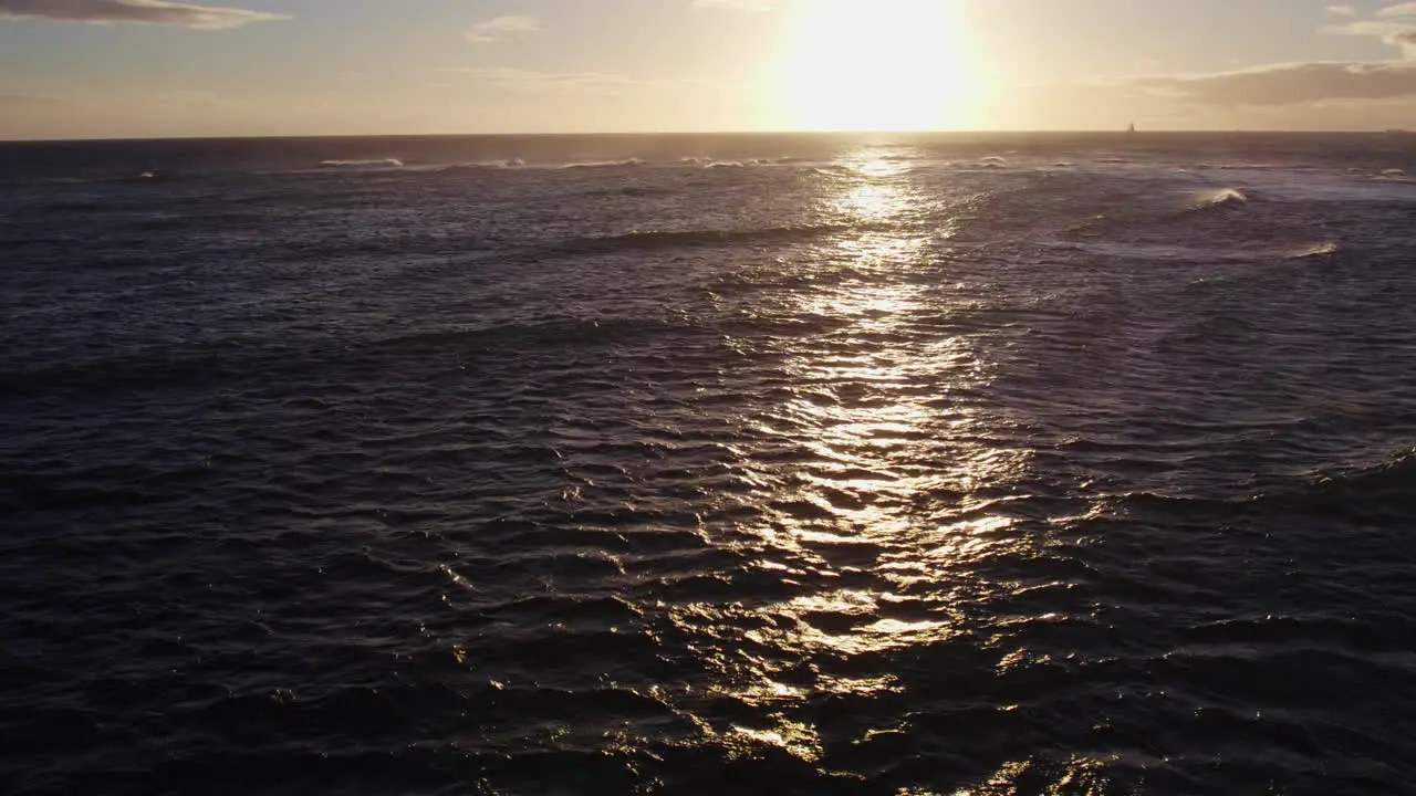 drone shot of the setting sun shining across the rippling ocean waves as the reflective rays follow the camera movement