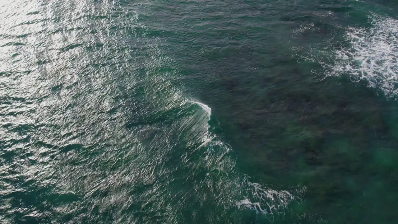 a drone swoops down to the crystal clear green water of the Pacific ocean as white capped waves break before the shore on the island of Oahu