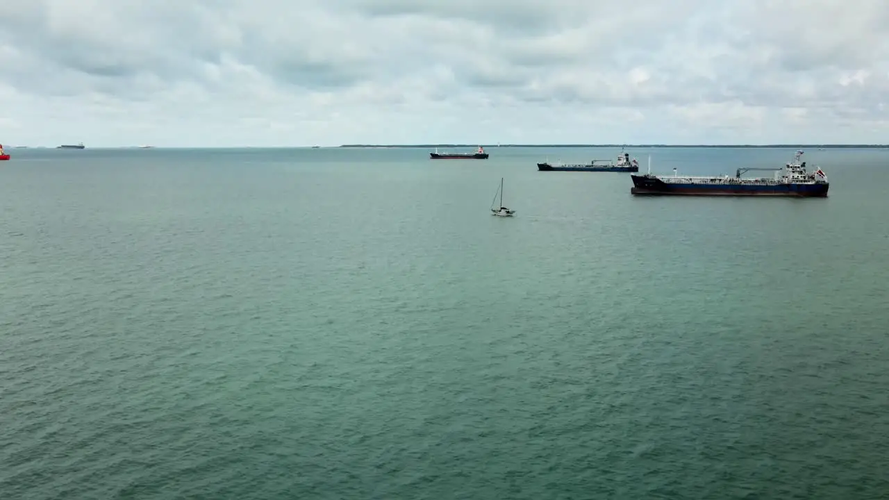 Small Sailboat sails in the Indian Ocean close to Malaysia between Many Large Cargo Ships