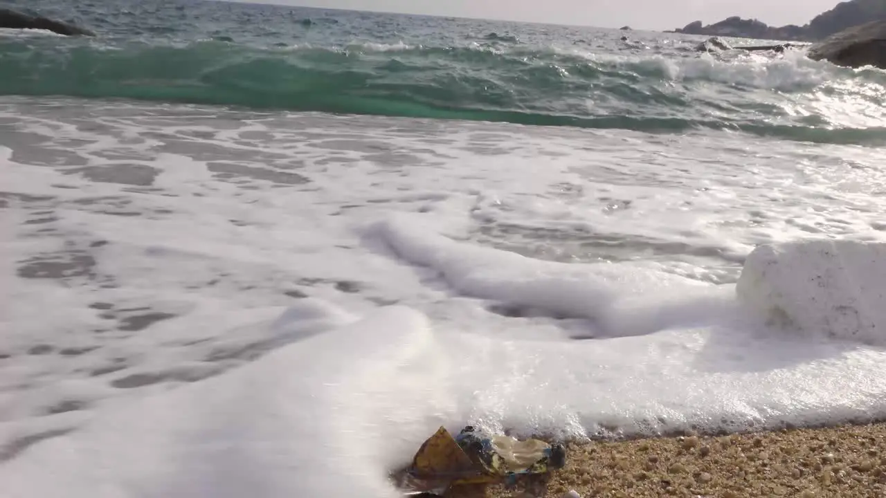 Hush wave washing over plastic trash on beach Low angle parallel static 4K side shot